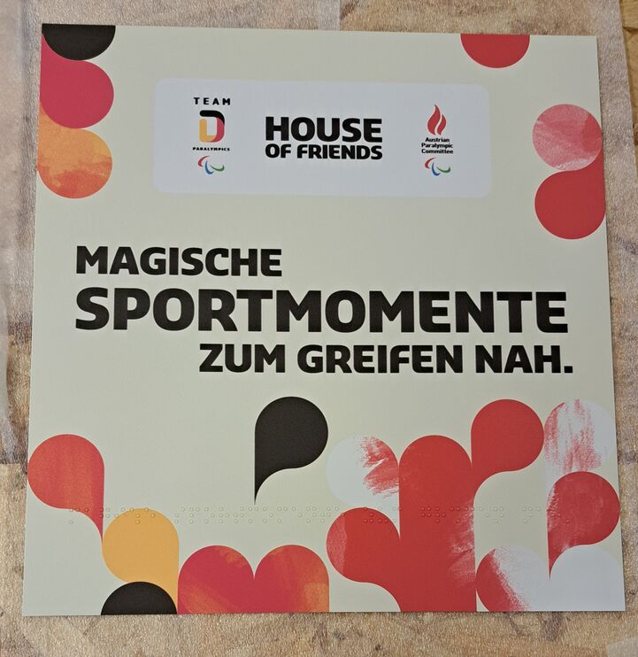Quadratisches Schild mit Brailleschrift und Großdruck "Magische Sportmomete zum Greifen nah", rote, gelbe und schwarze Tropfen
