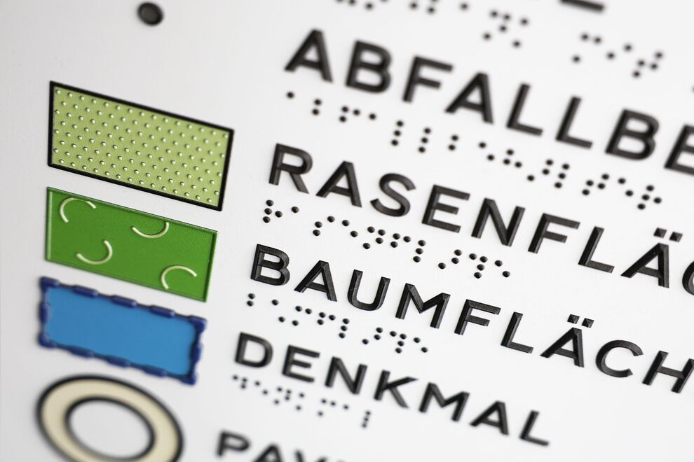 Detail der tastbaren Legende: Symbole, Groß- und Brailleschrift mit Braillelack