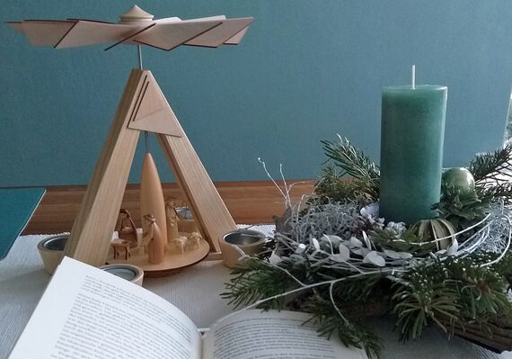 Aufgeschlagenes Buch im Vordergrund, dahinter eine Pyramide und ein Weihnachtsgesteck