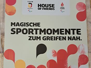 Quadratisches Schild mit Brailleschrift und Großdruck "Magische Sportmomete zum Greifen nah", rote, gelbe und schwarze Tropfen