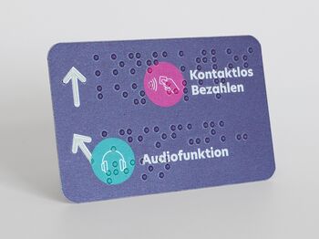 Rechteckiges, lilafarbenes Schild mit verschiedenen Piktogrammen und Brailleschrift im EC-Karten-Format