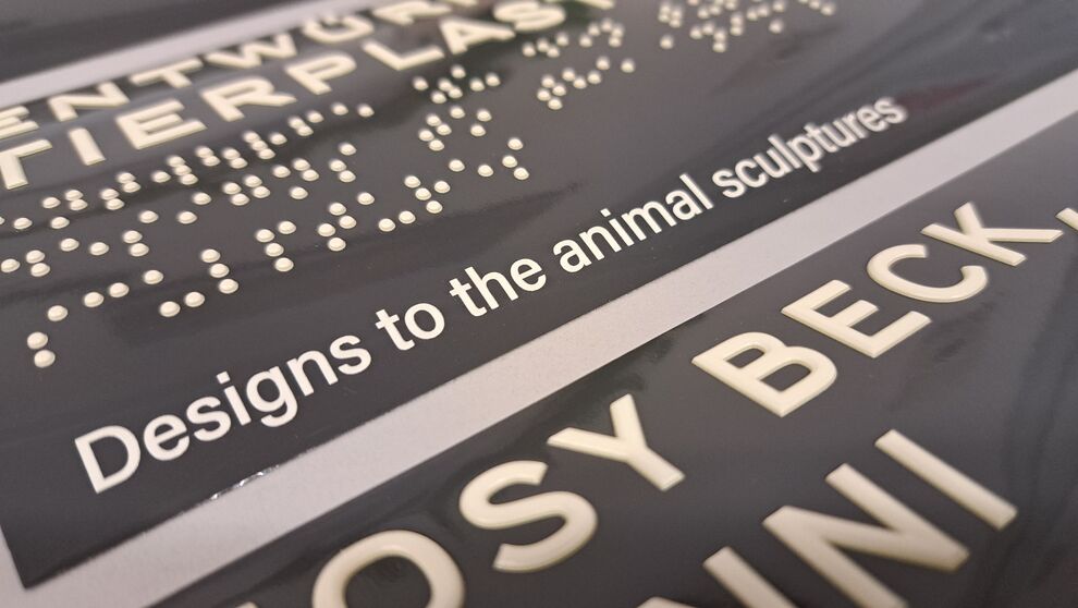 Detailansicht eines Aufklebeschildes mit taktiler Profilschrift und Brailleschrift