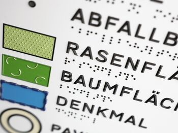 Detail der tastbaren Legende: Symbole, Groß- und Brailleschrift mit Braillelack
