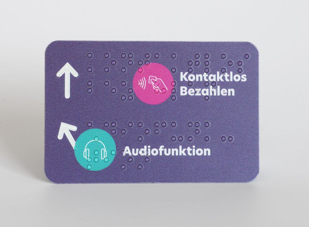 Rechteckiges, lilafarbenes Schild mit verschiedenen Piktogrammen und Brailleschrift im EC-Karten-Format