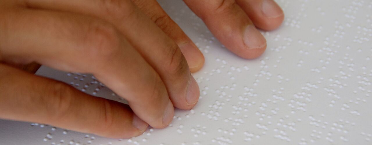 Zwei Hände über Brailleschriftbogen