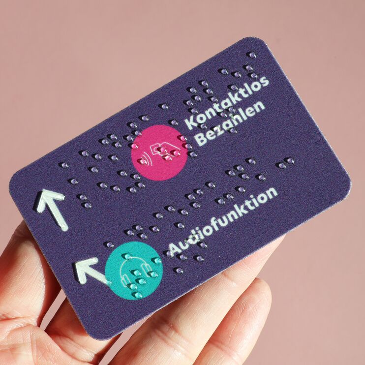 Rechteckiges, lilafarbenes Schild mit verschiedenen Piktogrammen und Brailleschrift im EC-Karten-Format