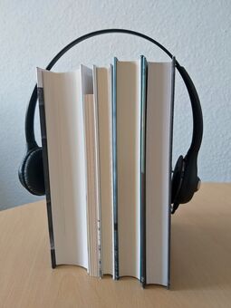 Stehende Bücher, die von den Ohrmuscheln eines Kopfhörers umfasst werden.