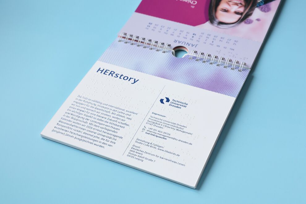 Liegender aufgeklappter Kalender mit unten Text in Schwarz- und Brailleschrift, oben angeschnittenes Foto