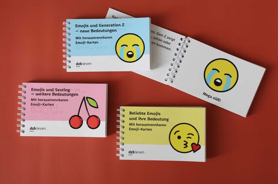 Vier rechteckige, kleine Ringbücher vor roten Hintergrund, das hintere ist aufgeschlagen