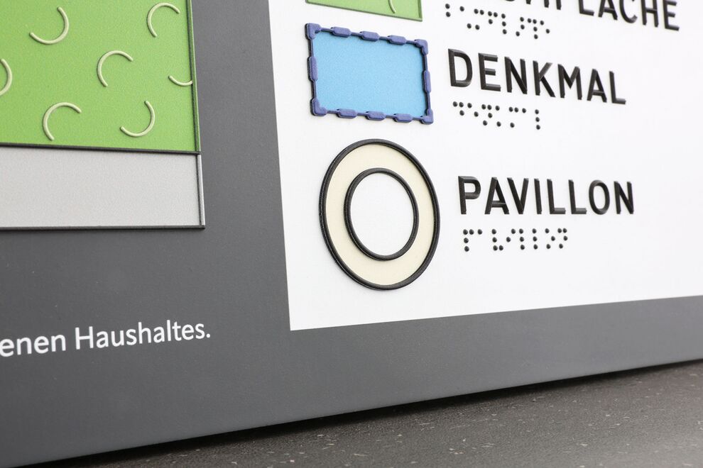 Detail der tastbaren Legende: Symbol und Brailleschrift mit Braillelack