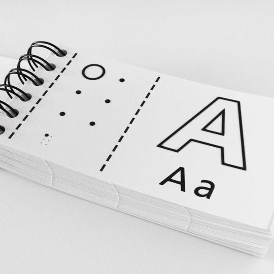 Aufgeschlagenes kleines Ringbuch mit dem Buchstaben A in Schwarzschrift und in Brailleschrift (Sechs-Punkte-Form)