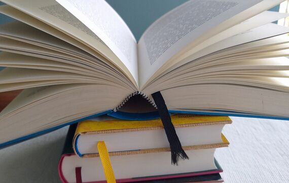 Ein aufgeschlagenes Buch liegt auf zwei Büchern mit Lesebändchen