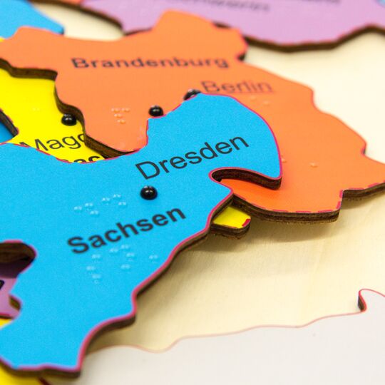 Farbige Puzzleteile des Deutschlandpuzzle (Sachsen, Brandenburg) auf Unterlage