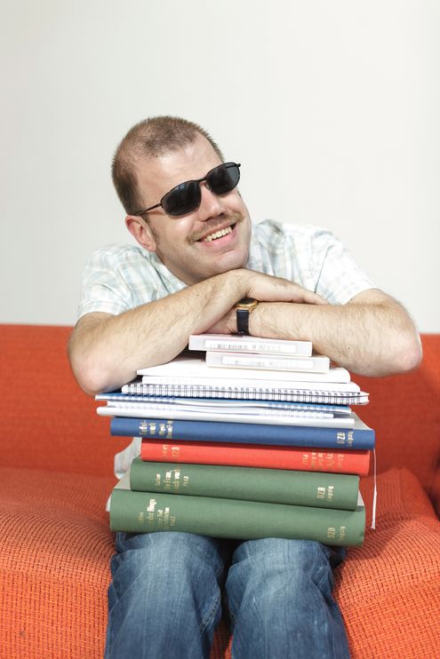 Sitzender Mann mit Brille stützt seine Arme auf einen Stapel Braillebücher
