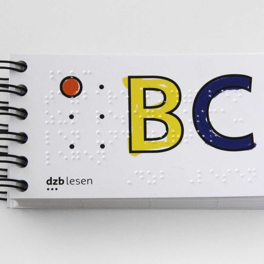 Kleines Ringbuch mit einem A in einer Sechs-Punkte-Form und BC in Schwarzschrift, unterlegt von Brailleschrift