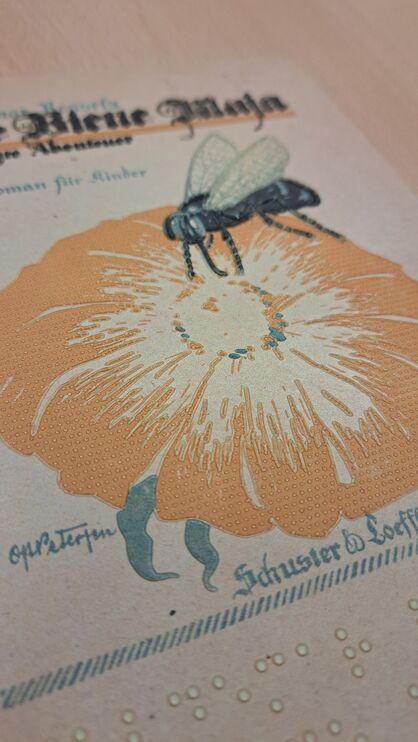 Detail vom taktilen Buchcover "Die Biene Maja", Illustration: Biene auf Blüte, darunter Brailleschrift