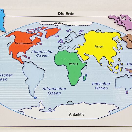Kunststoffplatte mit Kontinenten als Puzzle-Teile, einige liegen außerhalb der Platte