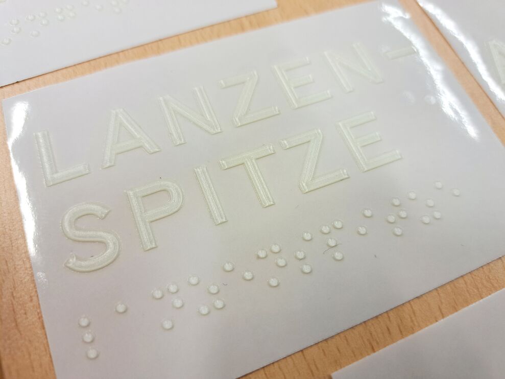 Transparenter taktiler Aufkleber mit weißer Profil- und Brailleschrift (Text: Lanzenspitze)
