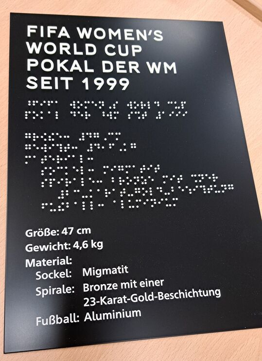 schwarzes, rechteckiges Schild mit weißer Profilschrift und Brailleschrift