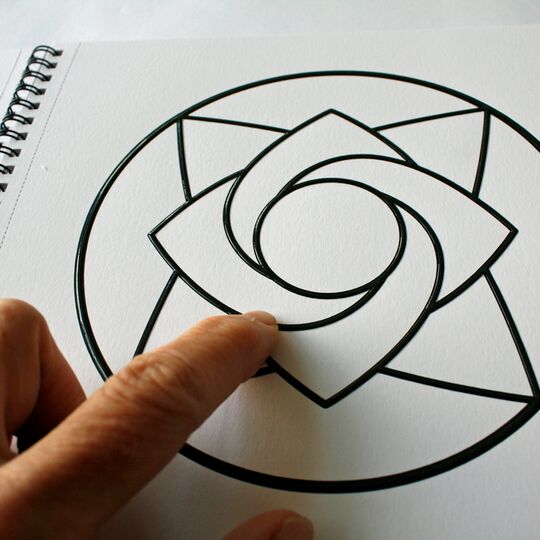 Aufgeschlagenes Ringbuch mit Mandala zum Ausmalen, ein Finger ertastet das Motiv